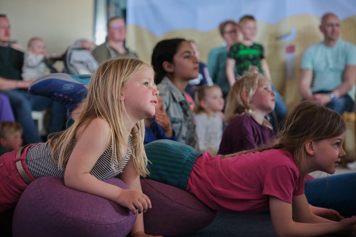 Kinderen liggen en zitten op kussens en kijken vol aandacht naar de voorstelling